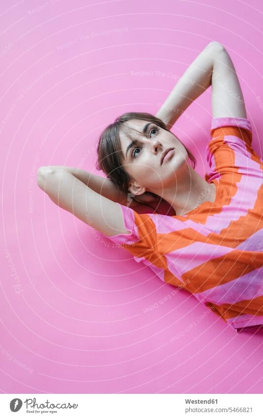 Frau liegt auf rosa Hintergrund mit Händen hinter dem Kopf und denkt pink pinkfarben liegen liegend nachdenken überlegen Hand hinter dem Kopf