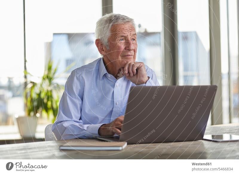 Porträt eines nachdenklichen älteren Mannes, der am Tisch mit Laptop sitzt und in die Ferne schaut Senior ältere Männer älterer Mann Senioren sitzen sitzend
