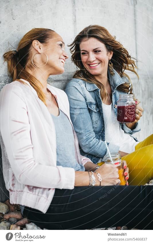 Zwei Freundinnen trinken Smoothies im Freien und haben Spaß Spass Späße spassig Spässe spaßig Freunde Freundschaft Kameradschaft Getränk Getraenk Getränke