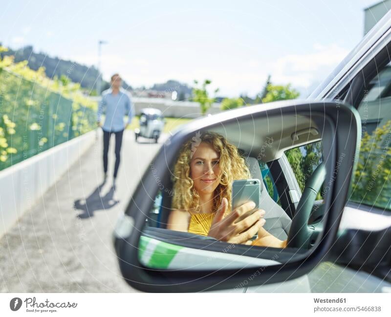 Lächelnde junge Frau benutzt Handy im Elektroauto Auto Wagen PKWs Automobil Autos Elektromobil Elektromobile Elektroautos weiblich Frauen Mobiltelefon Handies
