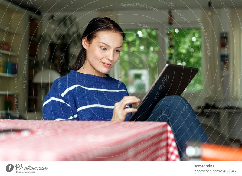 Junge Frau sitzt zu Hause und benutzt ein digitales Tablet Tisch Tische Tablet Computer Tablet-PC Tablet PC iPad Tablet-Computer benutzen benützen Smart Home