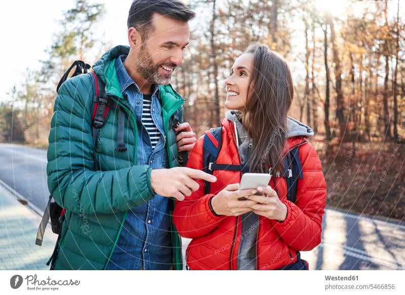 Glückliches Paar Überprüfung Smartphone auf einer Straße in den Wäldern während Rucksacktour Pärchen Paare Partnerschaft Ausflug Ausflüge Kurzurlaub Ausfluege