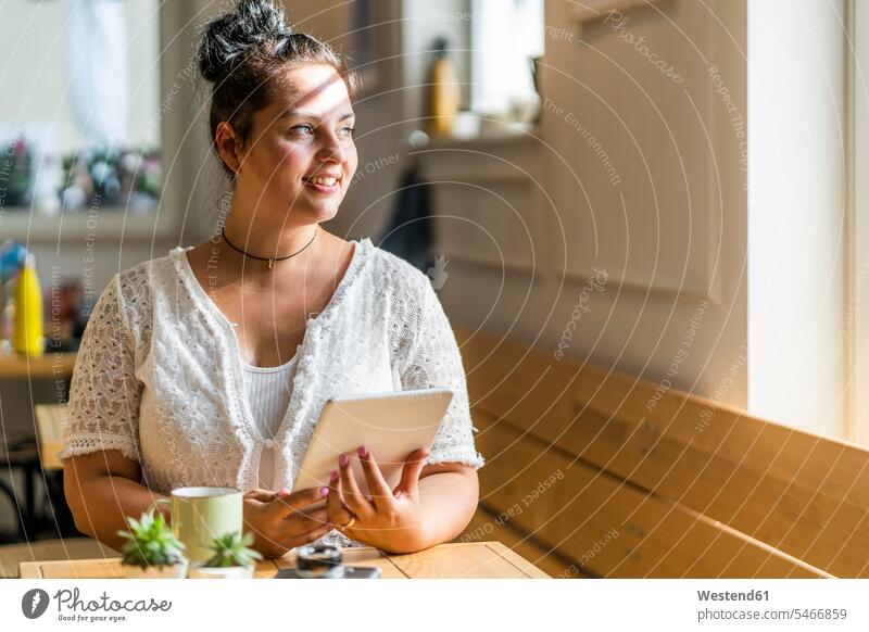 Nachdenkliche junge Frau mit digitalem Tablett sitzt am Tisch im Café Farbaufnahme Farbe Farbfoto Farbphoto Innenaufnahme Innenaufnahmen innen drinnen