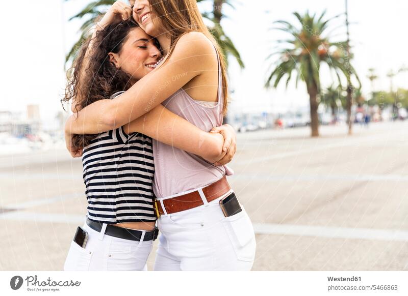 Zwei glückliche Freundinnen umarmen und umarmen sich auf der Promenade mit Palmen Promenaden knuddeln Glück glücklich sein glücklichsein Umarmung Umarmungen