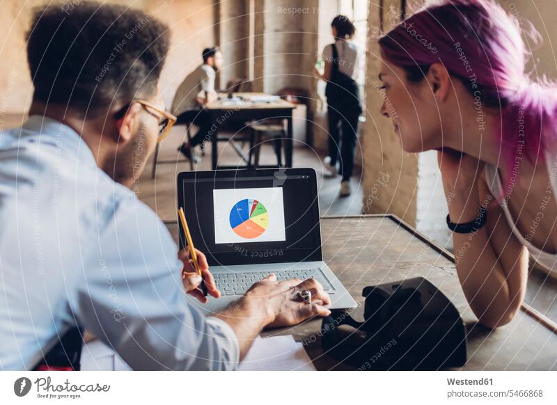 Zwei kreative Geschäftsleute beim Hantieren mit Diagrammen auf einem Laptop-Bildschirm im Loft-Büro Job Berufe Berufstätigkeit Beschäftigung Jobs Tische Rechner