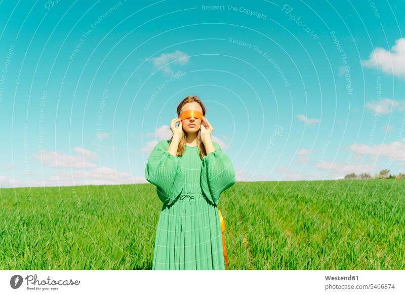 Junge Frau mit verbundenen Augen, die ein grünes Kleid trägt und in einem Feld steht Bänder Kleider anfassen Berührung entspannen relaxen Jahreszeiten Frühjahr