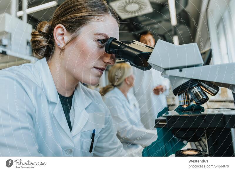 Assistentin analysiert Objektträger des menschlichen Gehirns, während sie mit einem Wissenschaftler im Hintergrund im Labor sitzt Menschen Personen zufällige