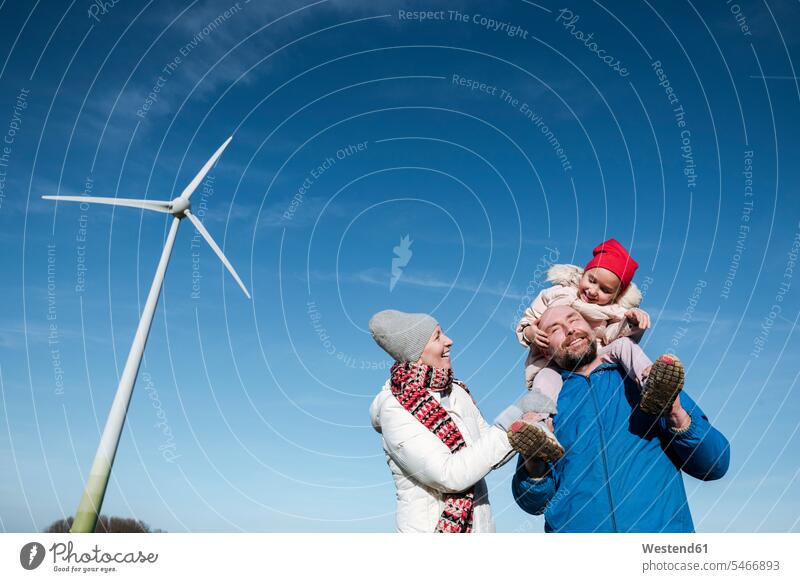 Glückliche Eltern mit kleiner Tochter gegen den Himmel mit Windrad im Hintergrund Umwelt- und Naturschutz Umweltthemen Umweltschutz Ökologie alternative Energie