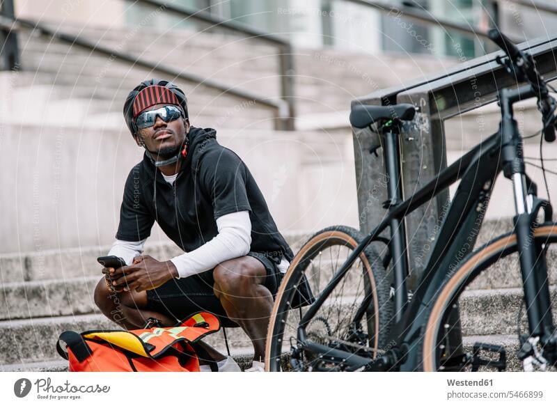 Stilvoller junger Mann mit Fahrrad, Smartphone und Kuriertasche in der Stadt Leute Menschen People Person Personen Afrikanisch Afrikanische Abstammung
