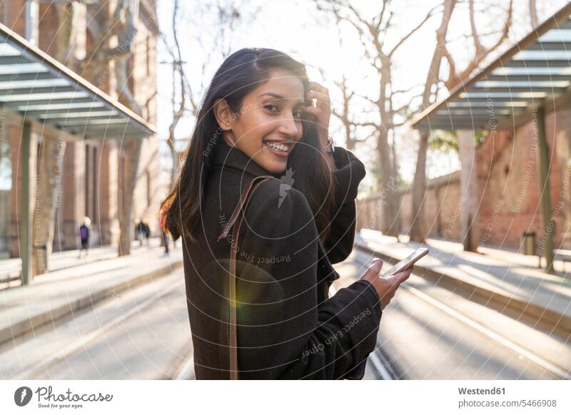 Porträt einer glücklichen jungen Frau mit Smartphone auf der Straßenbahnlinie Transport Transportwesen Bahnen Straßenbahnen Tram Trambahn Telekommunikation