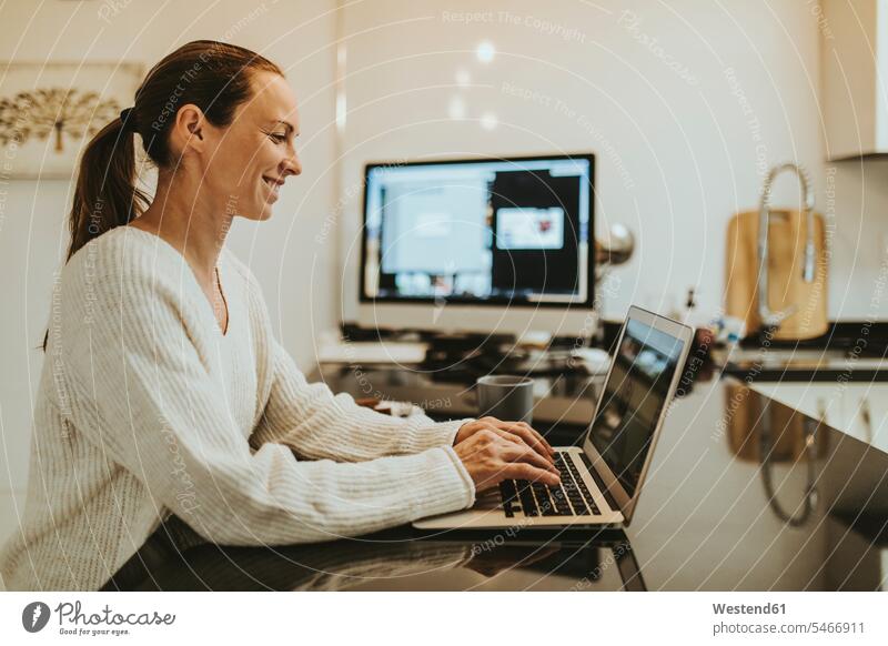 Frau bei Videoanruf mit Freundin über Laptop auf der Kücheninsel Farbaufnahme Farbe Farbfoto Farbphoto Verbindung verbunden Anschluss verbinden Zuhause