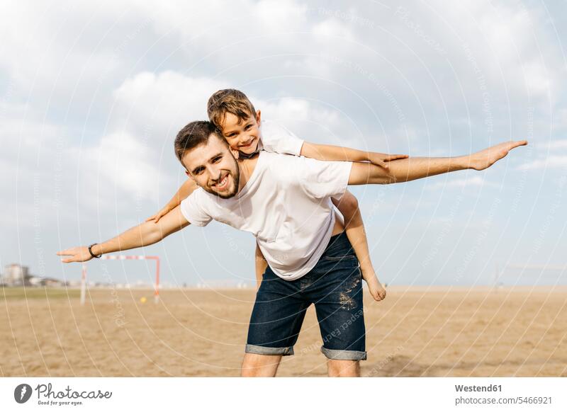 Mann trägt Junge huckepack am Strand T-Shirts Bälle Jubel sommerlich Sommerzeit begeistert Enthusiasmus enthusiastisch Überschwang Überschwenglichkeit freuen