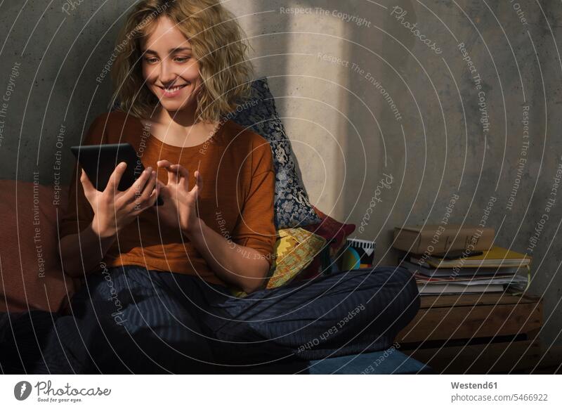 Porträt einer lächelnden jungen Frau, die mit einem E-Book-Reader auf dem Bett sitzt Europäer eine Person junge Frau 25-30 Jahre Innenaufnahme Deutschland