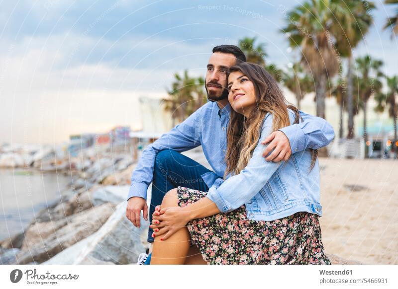Spanien, Barcelona, Ehepaar sitzt auf Felsen am Meer Paar Pärchen Paare Partnerschaft Gemeinsam Zusammen Miteinander Küste Küstenlandschaft sitzen sitzend