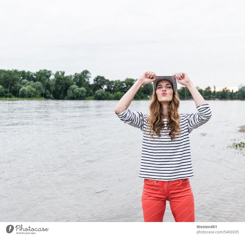 Verspielte Frau mit Wollmütze an einem Fluss, die schmollt Wollmützen Strickmütze Strickmützen Fluesse Fluß Flüsse Kussmund weiblich Frauen verspielt