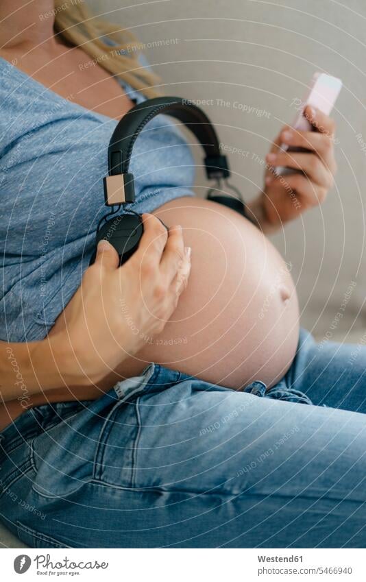 Mittelteil einer schwangeren Frau, die Kopfhörer an ihren Bauch hält Bäuche weiblich Frauen Kopfhoerer halten Schwangere schwangere Frau Mensch Menschen Leute