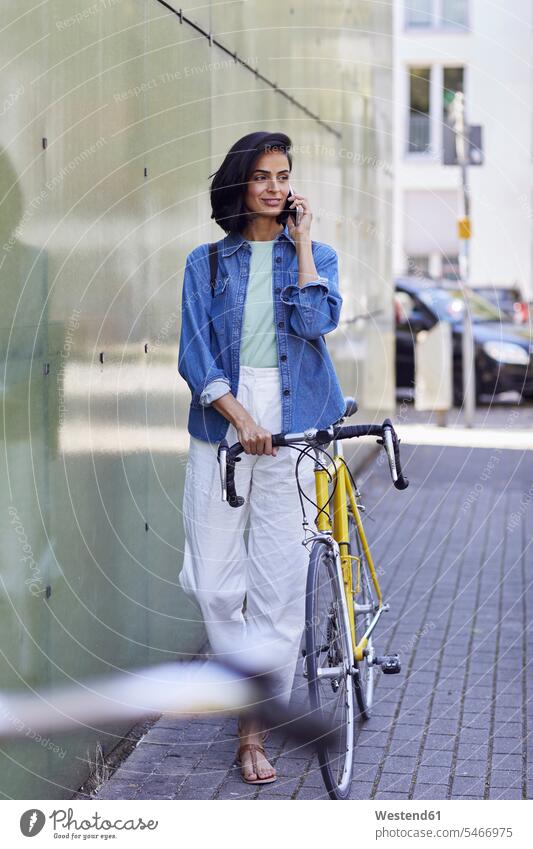 Pendlerin, die mit einem Smartphone telefoniert, während sie in der Stadt mit dem Fahrrad auf der Straße steht Farbaufnahme Farbe Farbfoto Farbphoto Deutschland