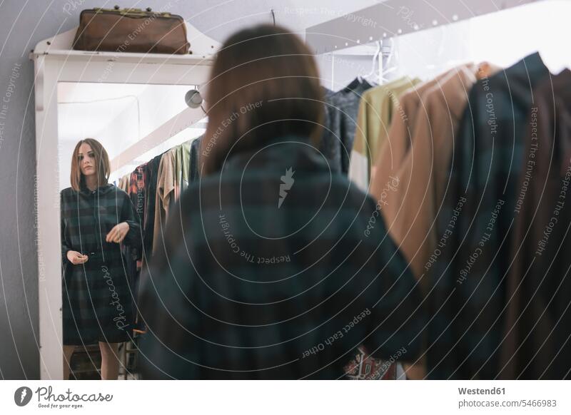 Junge Frau probiert Kleid aus, während sie im Spiegel in ein Design-Studio schaut Farbaufnahme Farbe Farbfoto Farbphoto Freizeitbeschäftigung Muße Zeit