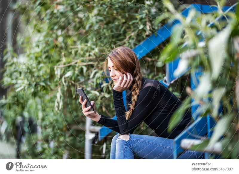 Lächelnde Frau sitzt auf der Treppe und schaut auf ihr Smartphone iPhone Smartphones Treppenaufgang sitzen sitzend weiblich Frauen ansehen Handy Mobiltelefon