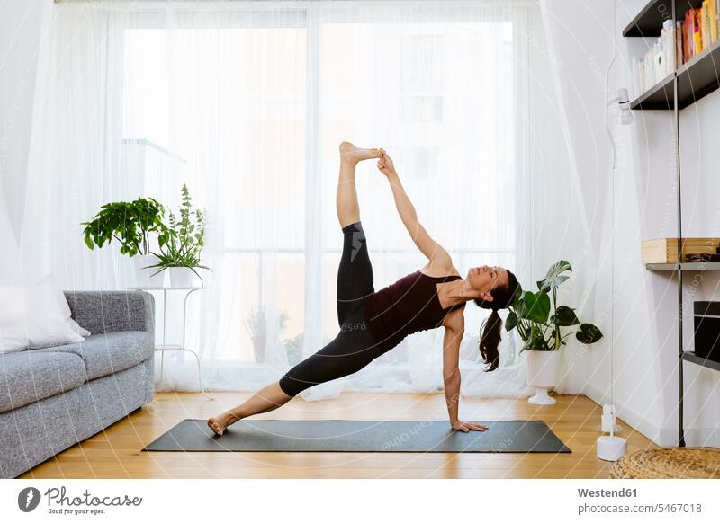 Frau, die zu Hause Yoga praktiziert Gardine Gardinen Vorhänge Couch Couches Liege Sofas ausüben trainieren Übung daheim fit gesund Gesundheit anpassungsfähig