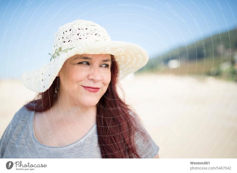 Porträt einer lächelnden Frau mit Sommerhut am Strand Hut Hüte Sommerhüte Sommerhuete Portrait Porträts Portraits Beach Straende Strände Beaches tragen anhaben