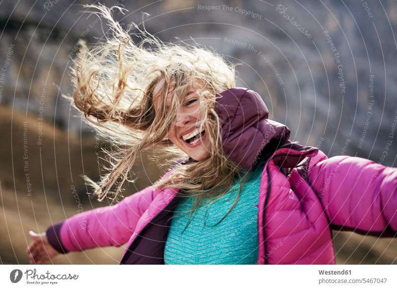 Glückliche junge Frau lehnt in den Bergen gegen den Wind lachen weiblich Frauen Portrait Porträts Portraits Windstoß windig Wanderer wandern Wanderung positiv