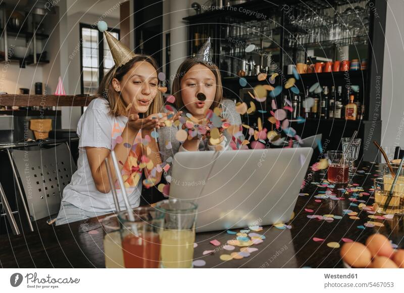 Fröhliche Freunde blasen Konfetti bei Videokonferenzen über Laptop, während sie zu Hause sitzen Farbaufnahme Farbe Farbfoto Farbphoto Deutschland Innenaufnahme
