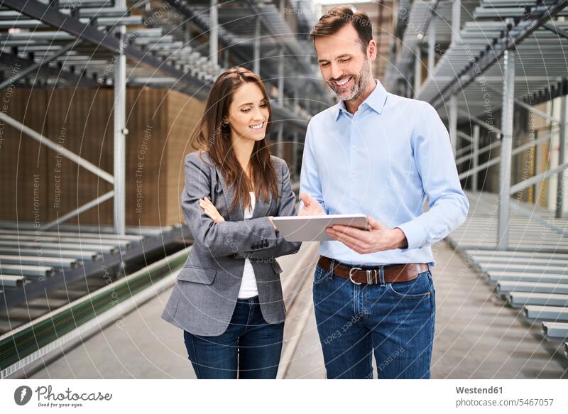 Lächelnde Geschäftsfrau und Geschäftsmann mit Tablette in einer Fabrik Job Berufe Berufstätigkeit Beschäftigung Jobs geschäftlich Geschäftsleben Geschäftswelt