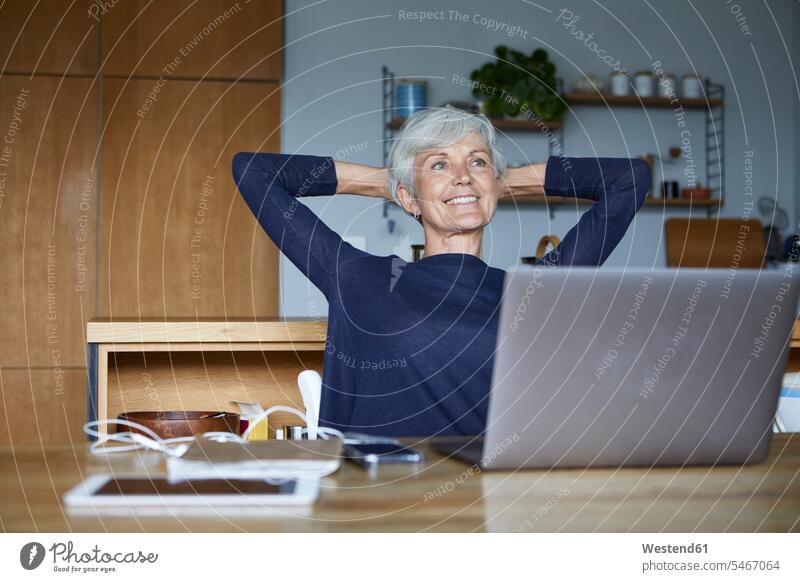 Lächelnde ältere Frau mit Händen hinter dem Kopf entspannt zu Hause sitzend Farbaufnahme Farbe Farbfoto Farbphoto Innenaufnahme Innenaufnahmen innen drinnen Tag