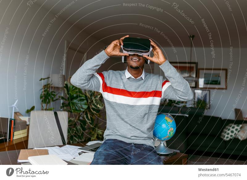 Geschäftsmann benutzt Virtual-Reality-Headset, während er zu Hause am Schreibtisch sitzt Farbaufnahme Farbe Farbfoto Farbphoto Innenaufnahme Innenaufnahmen