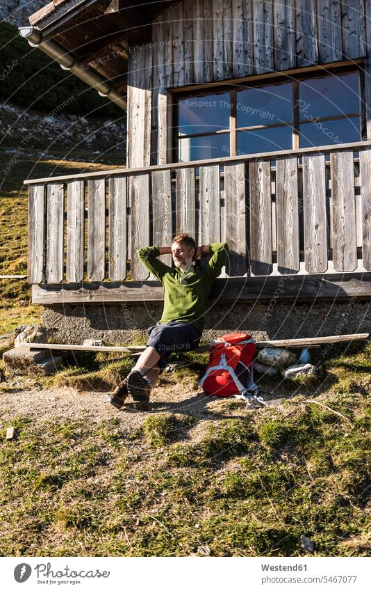 Älterer Mann entspannt sich auf einer Berghütte und genießt die Sonne Rucksack Rucksäcke Berghütten Berghuette Hütte bergsteigen Bergsteiger Pause Pause machen