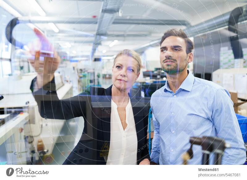Zuversichtliche Geschäftsfrau plant mit jungem Ingenieur, während sie auf die Glasschnittstelle in der Fabrik zeigt Farbaufnahme Farbe Farbfoto Farbphoto