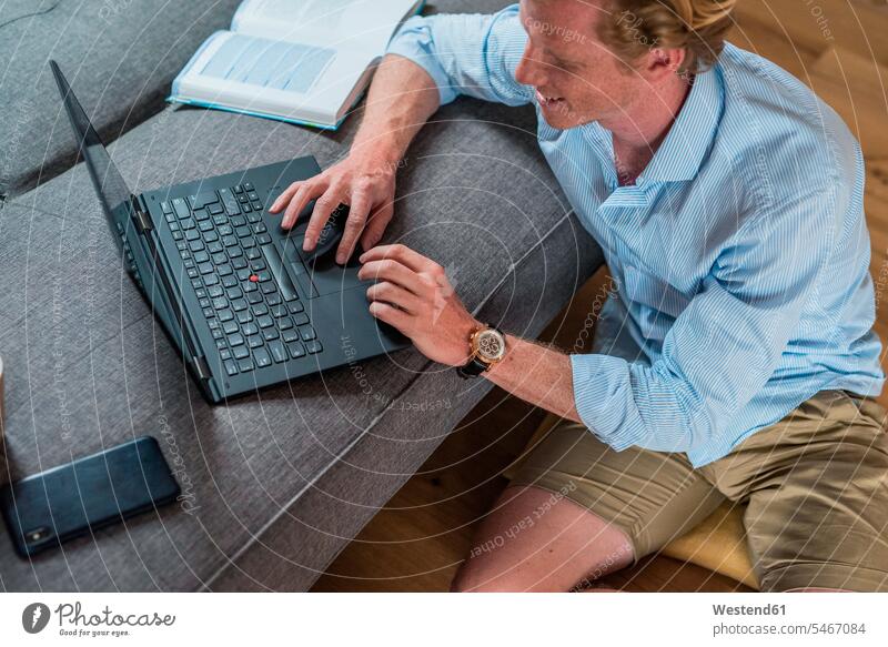 Männlicher Freiberufler arbeitet am Laptop im Wohnzimmer Farbaufnahme Farbe Farbfoto Farbphoto Innenaufnahme Innenaufnahmen innen drinnen Tag Tageslichtaufnahme