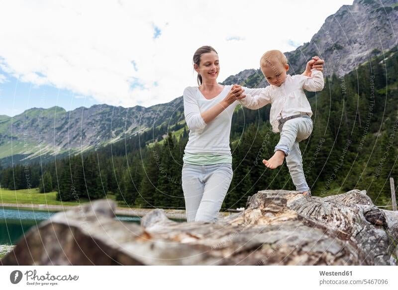 Deutschland, Bayern, Oberstdorf, Mutter hilft kleiner Tochter beim Balancieren auf einem Baumstamm Mamas Mami Mutti Mütter Muetter Mamis Muttis balancieren