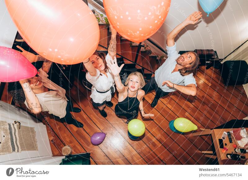 Fröhliche Freunde tanzen mit bunten Luftballons während einer Party zu Hause Farbaufnahme Farbe Farbfoto Farbphoto Innenaufnahme Innenaufnahmen innen drinnen