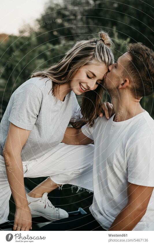 Porträt eines jungen lächelnden Paares, Mann küsst sie auf die Stirn T-Shirts Arm umlegen Umarmung Umarmungen abends freuen Glück glücklich sein glücklichsein