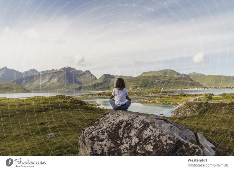 Junge Frau sitzt auf einem Felsen, schaut auf die Aussicht, meditiert, Lappland, Norwegen junge Frau junge Frauen Meditation meditieren nachdenken überlegen