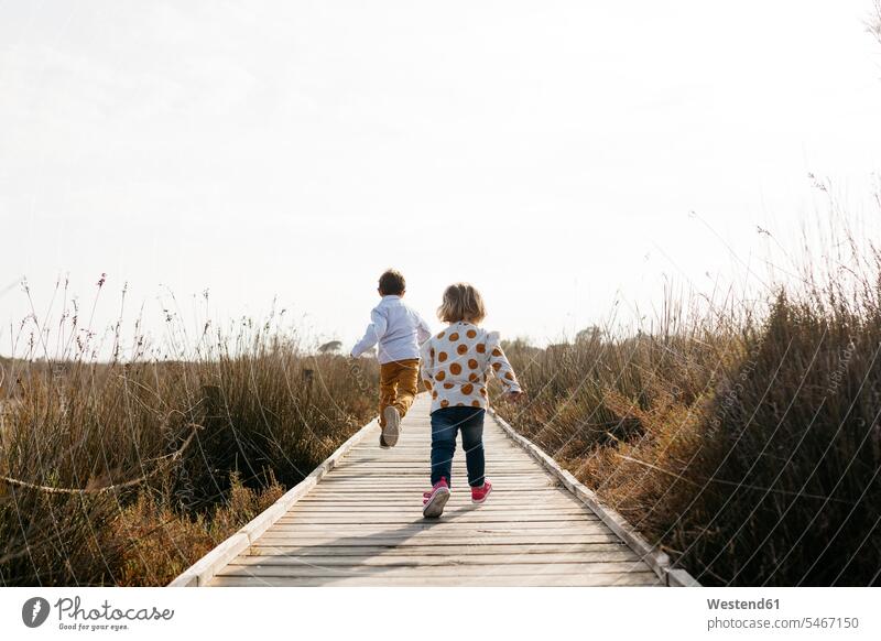Rückenansicht von zwei kleinen Kindern, die auf der Strandpromenade laufen Europäer Kaukasier Europäisch kaukasisch Zusammengehörigkeit Verbundenheit Bindung