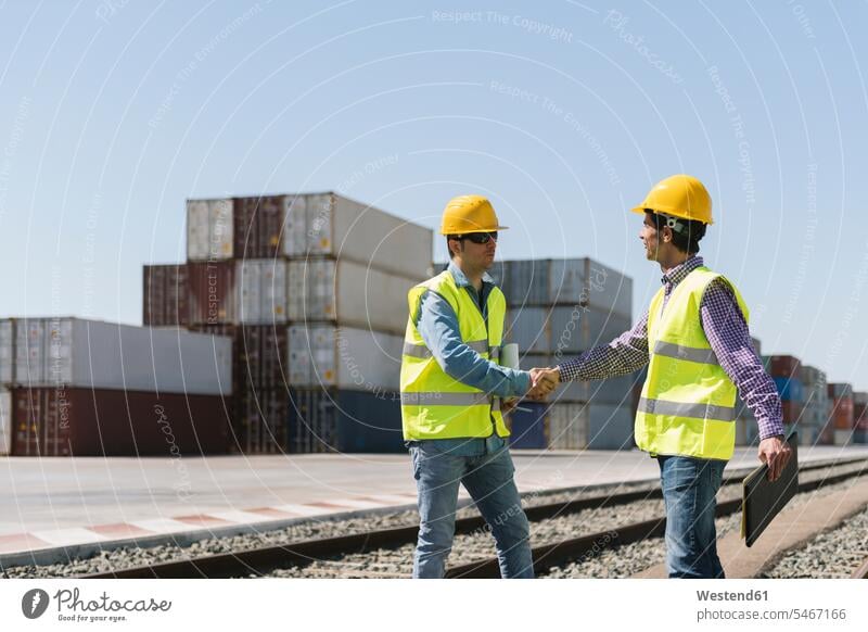 Arbeiter beim Händeschütteln auf Bahngleisen in der Nähe von Frachtcontainern auf einem Industriegelände Spanien Sachverstand Sachkenntnis Kompetenz Know-How
