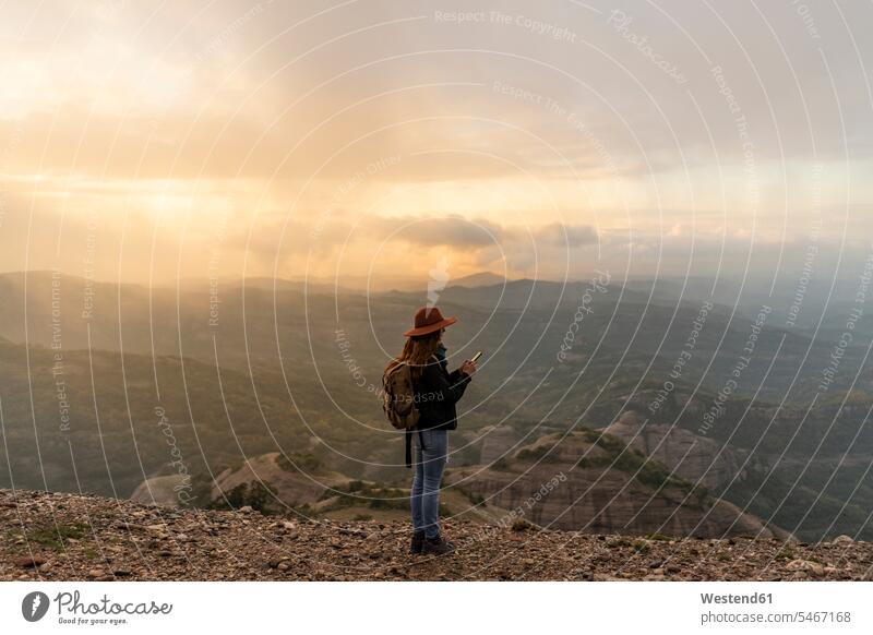 Frau mit Rucksack, stehend auf einem Berg, mit Blick auf die Aussicht, mit Smartphone Rucksäcke Aussicht bewundern die Aussicht bewundern Blick in die Ferne