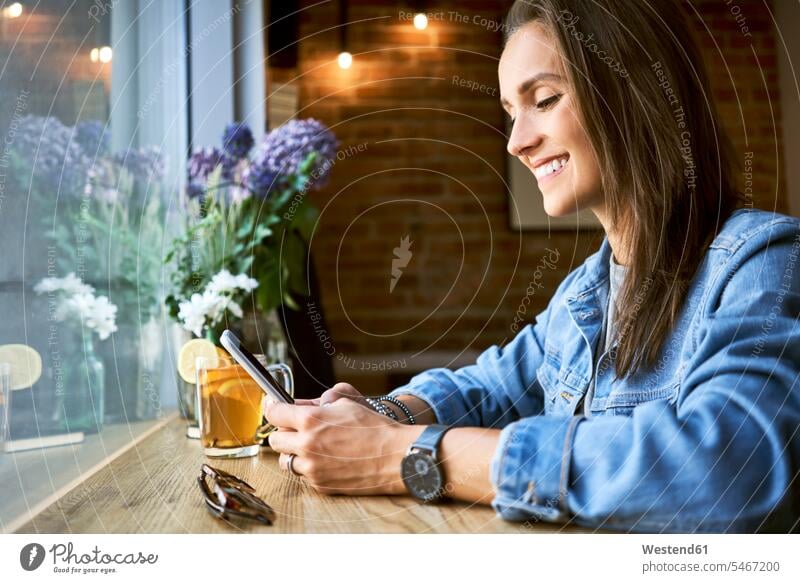Lächelnde junge Frau mit Telefon im Café Cafe Kaffeehaus Bistro Cafes Cafés Kaffeehäuser lächeln Handy Mobiltelefon Handies Handys Mobiltelefone weiblich Frauen
