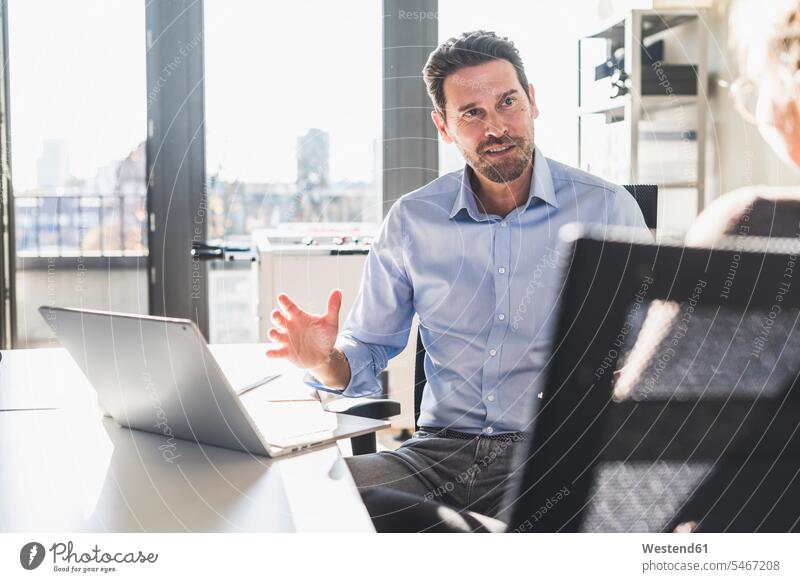 Geschäftsmann benutzt Laptop während einer Diskussion mit einem Kollegen im Büro Farbaufnahme Farbe Farbfoto Farbphoto Innenaufnahme Innenaufnahmen innen