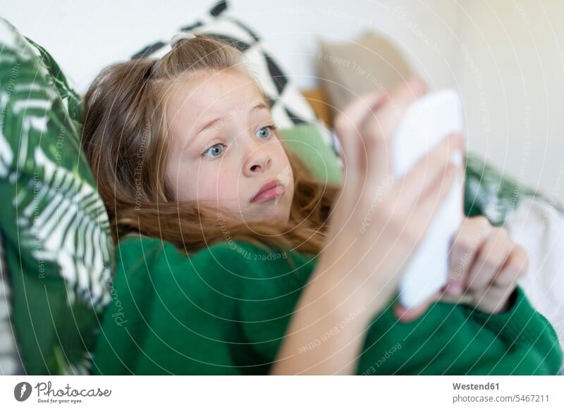 Porträt eines Mädchens mit grünem Pullover, das auf dem Bett liegt und auf sein Handy starrt Leute Menschen People Person Personen Europäisch Kaukasier