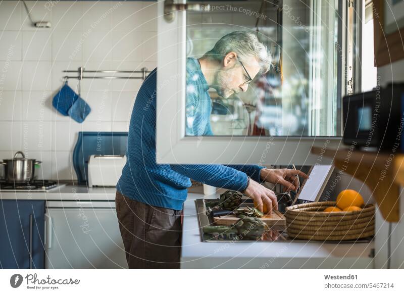 Erwachsener Mann bereitet Artischocke in seiner Küche mit Hilfe eines digitalen Tabletts zu Leute Menschen People Person Personen Alleinstehende Alleinstehender