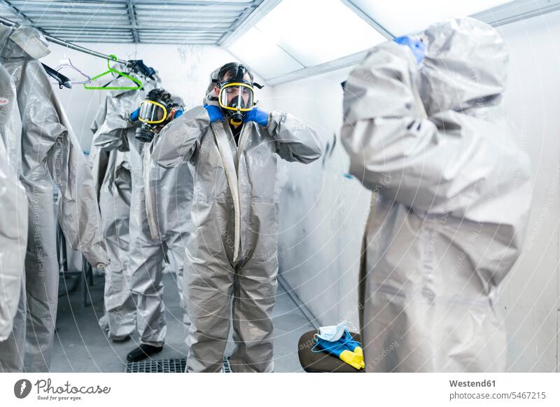 Team von Sanitärarbeitern mit Schutzanzügen und Gasmasken, die in der Umkleidekabine stehen Farbaufnahme Farbe Farbfoto Farbphoto Coronavirus Covid-19 Virus