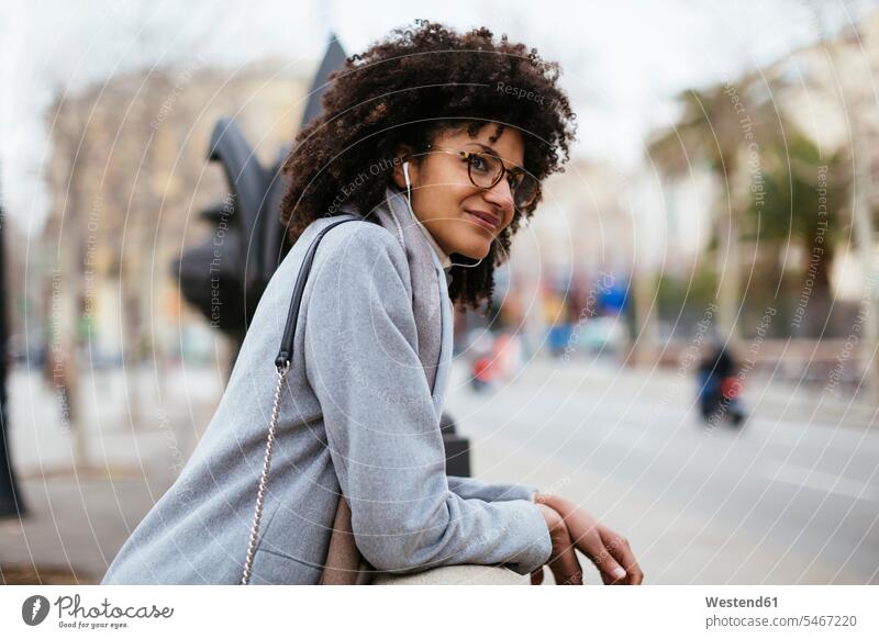 Spanien, Barcelona, lächelnde Frau mit Kopfhörern in der Stadt, die wegschaut wegsehen Blick zur Seite wegschauen staedtisch städtisch weiblich Frauen Ohrhörer