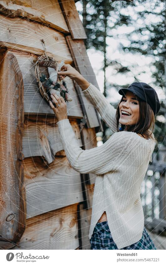 Glückliche junge Frau schmückt Holzhaus mit Weihnachtsdekoration weiblich Frauen Weihnachten Christmas X-Mas X mas Holzhäuser Holzhaeuser dekorieren glücklich