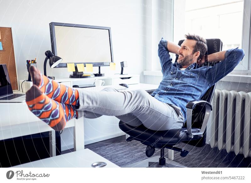 Entspannter Mann sitzt im Büro am Schreibtisch und schaut auf den Computerbildschirm entspannt entspanntheit relaxt Office Büros Männer männlich ansehen