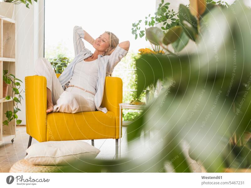 Porträt einer lächelnden reifen Frau, die sich zu Hause im Sessel entspannt Polster entspannen relaxen sitzend sitzt freuen geniessen Genuss zufrieden Farben