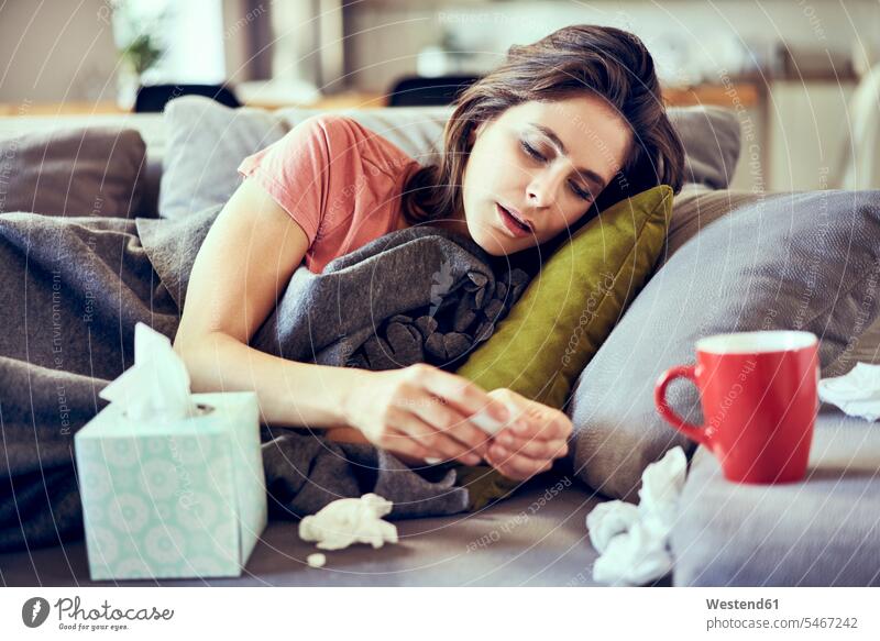 Porträt einer kranken jungen Frau, die auf einer Decke liegt und versucht, Tabletten gegen Erkältung zu nehmen Pille Pillen Erkaeltung Schnupfen Grippe